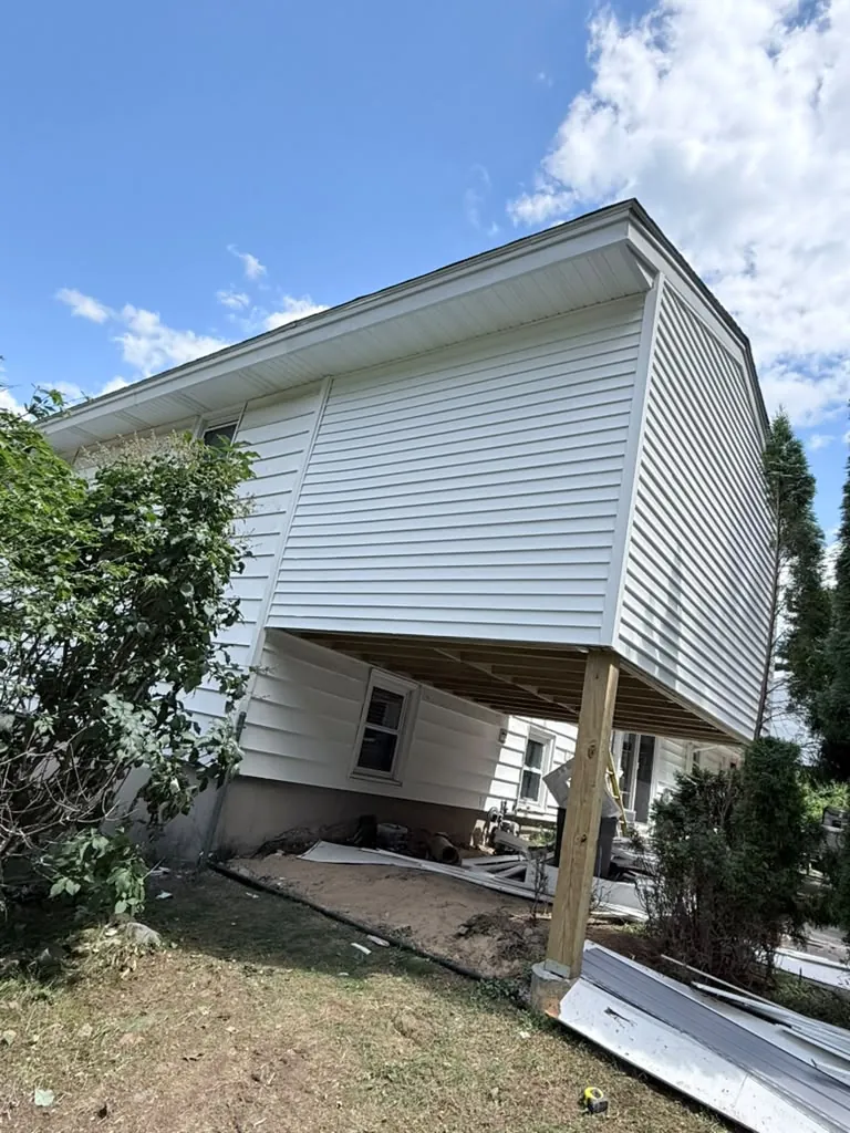 The finished addition sided in white, cantilevered over the yard on its posts