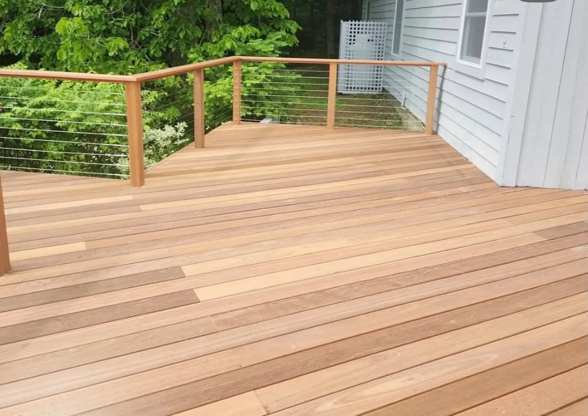 Finished hardwood deck with a cable railing on wood posts, against the white siding of the house
