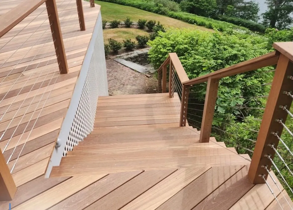 Hardwood deck stairs with cable railing turning down toward the garden and the water
