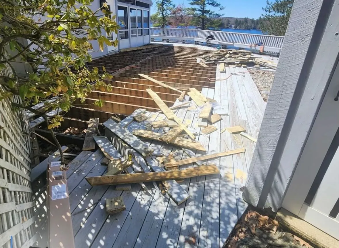 Old gray deck boards being pulled up over the framing, with the lake beyond the railing