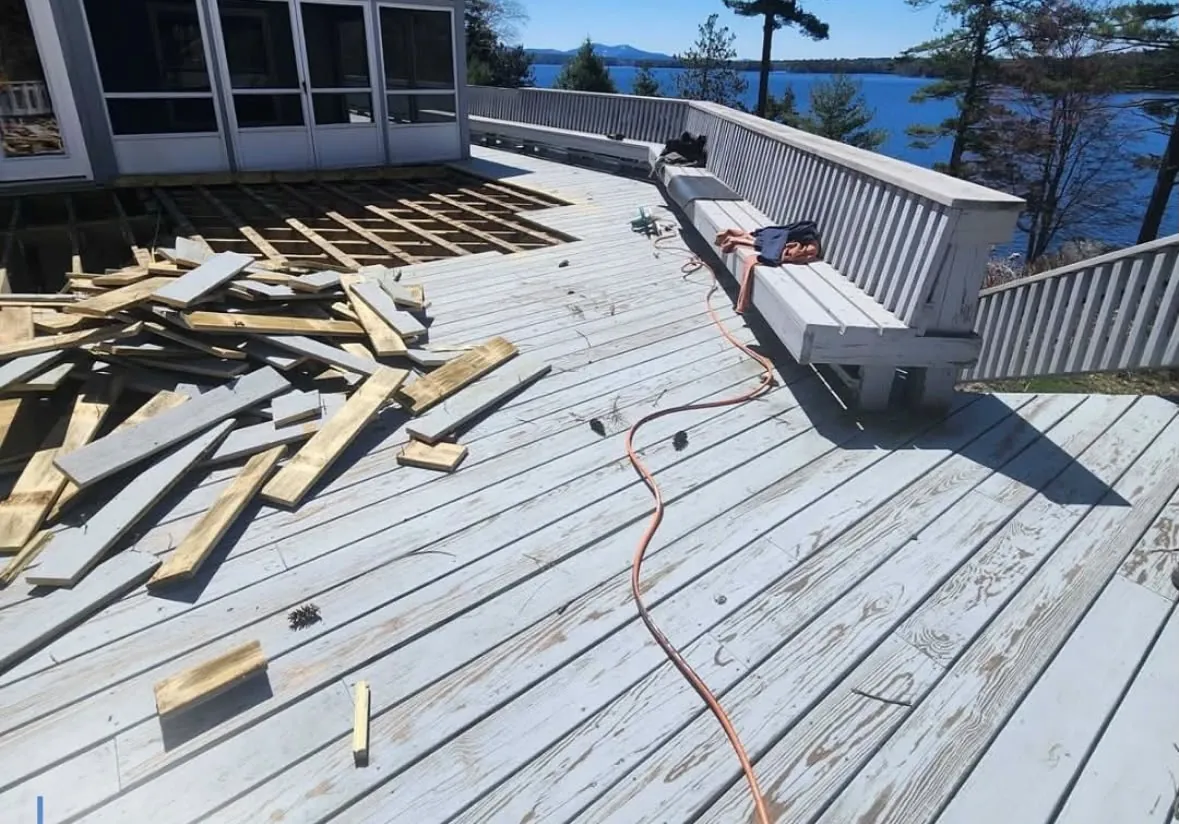 Deck stripped back to the joists with the old boards stacked, lake and treeline behind