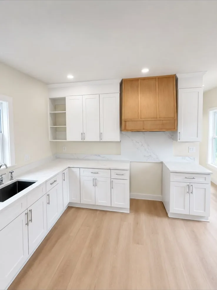 White shaker kitchen with a wood hood over the range wall and a marble-look backsplash