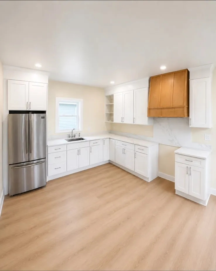 The finished kitchen from the doorway, with stainless fridge, open shelving and light plank flooring