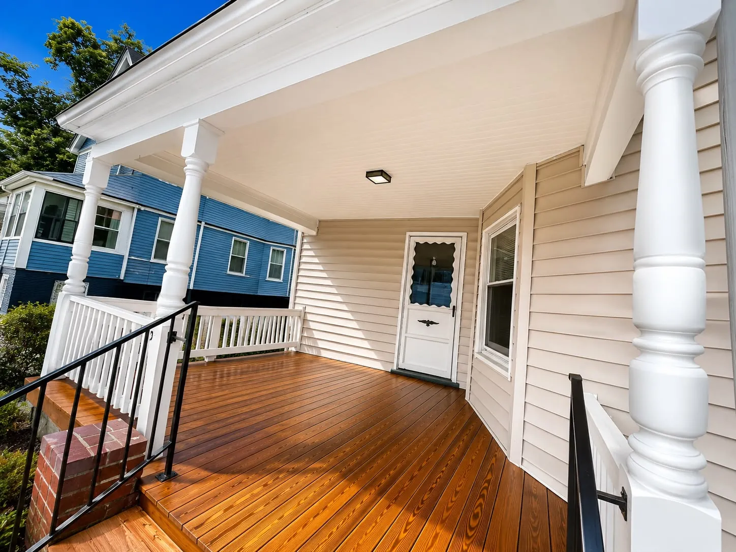 The finished porch floor in stained wood running to the front door, between white columns
