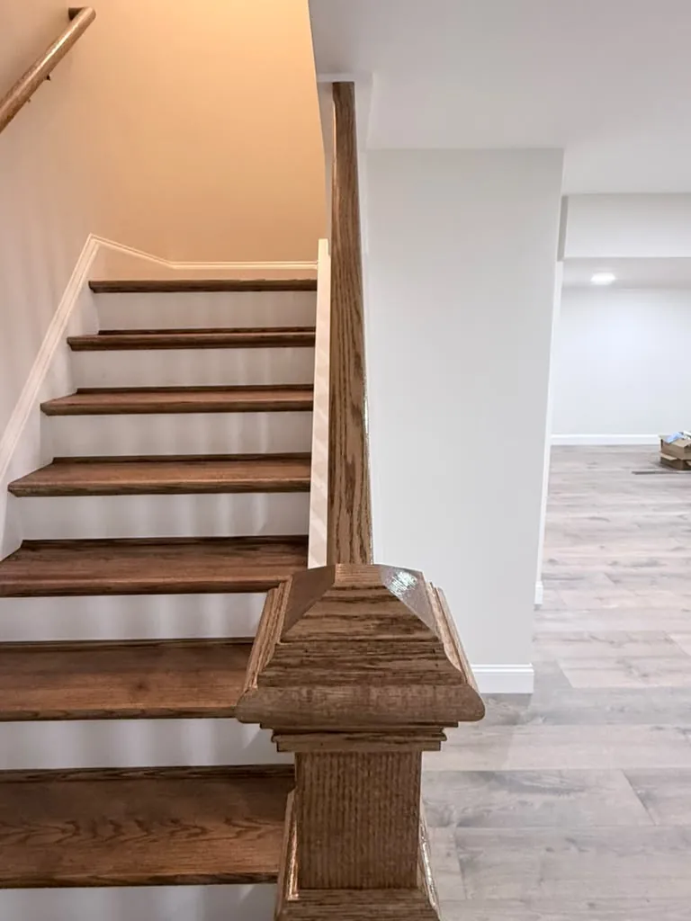 The finished stair opening onto the room, with the oak rail and white balusters
