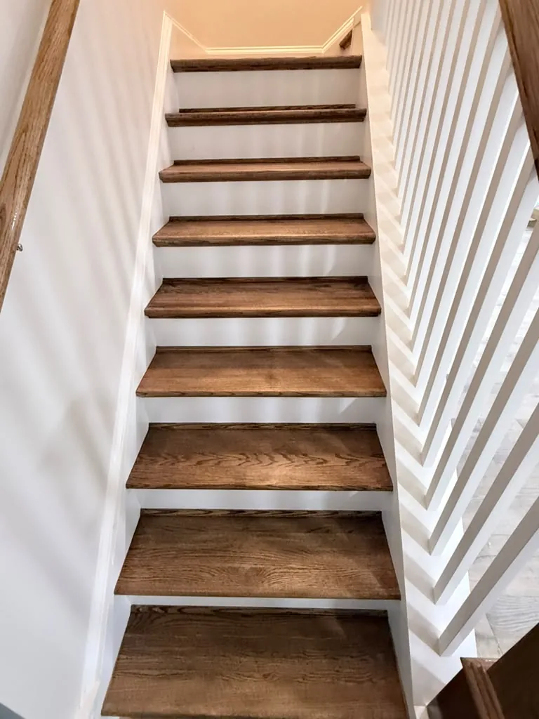 Oak stair treads with white risers and balusters, looking up the run